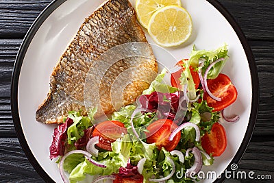 Tasty fried dorado fish fillet with fresh vegetable salad close-up on a plate. Horizontal top view Stock Photo