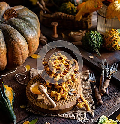 Tasty homemade pumpkin orange waffles on wooden board on brown rustic table with pumpkins Stock Photo