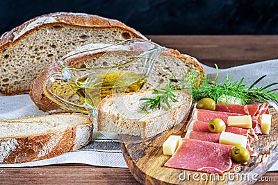 Tasty mediterranean food for snack. Olive oil in glass bowl, sliced integral bread, jamon, cheese and olives on the kitchen table Stock Photo