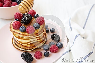 Tasty pancakes with berries and honey on a pink plate, side view. Stock Photo