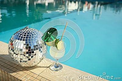 Tasty refreshing cocktail and shiny disco ball on edge of swimming pool. Party items Stock Photo