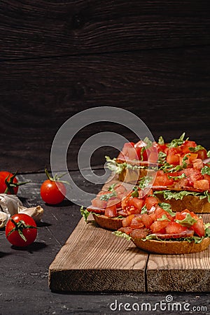 Tasty savory tomato Italian appetizers, or bruschetta, on slices of toasted baguette garnished with salad leaves, ham, chopped Stock Photo