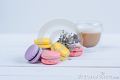 Tasty violet and yellow macarons and cup of latte and branch of fragrant lavender on white wooden background. Stock Photo