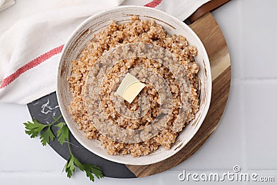 Tasty wheat porridge with butter and parsley in bowl on white tiled table, top view Stock Photo