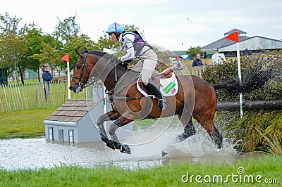 Tattersalls horse show in Ireland, horse galopping after obstacle in water with male rider, jockey rushing forward Editorial Stock Photo