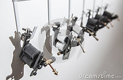 Tattoo coil ink machines hanging from hooks on white wall Stock Photo