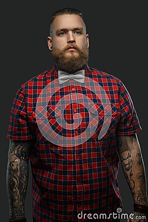 Tattooed bearded unformal male in red shirt and grey bow tie. Stock Photo