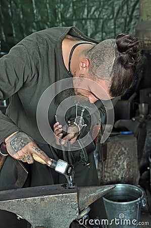 Tattooed blacksmith working with hammer on anvil Editorial Stock Photo
