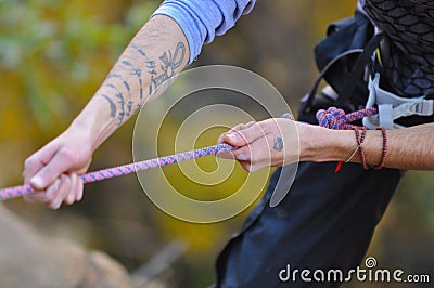 Tattooed climber grips the rope for abseiling down the mountain face Stock Photo