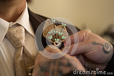 Tattooed hands pin burlap corsage on groom Stock Photo