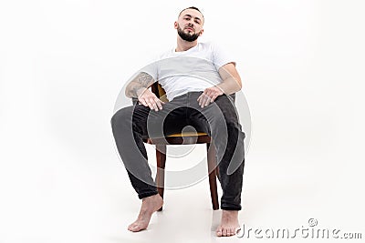 Tattooed handsome brunet, confident, bearded barefoot man sit relaxing like boss on chair like boss. Low angle view Stock Photo