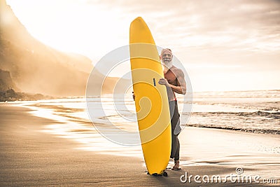 Tattooed senior surfer holding surf board on the beach at sunset - Happy old guy having fun doing extreme sport - Joyful elderly Stock Photo