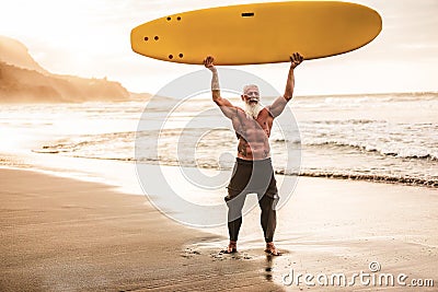 Tattooed senior surfer holding surf board on the beach at sunset - Happy old guy having fun doing extreme sport - Joyful elderly Stock Photo