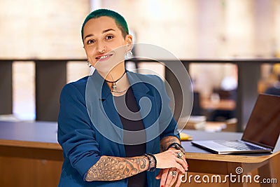 Tattooed woman with electric blue hair sits at desk with laptop Stock Photo