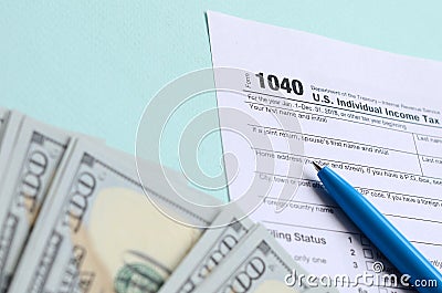 1040 tax form lies near hundred dollar bills and blue pen on a light blue background. US Individual income tax return Editorial Stock Photo