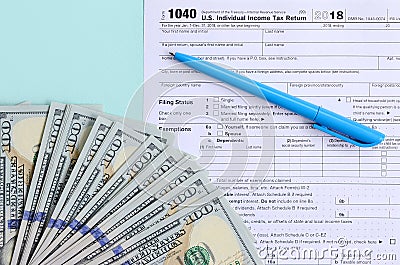 1040 tax form lies near hundred dollar bills and blue pen on a light blue background. US Individual income tax return Editorial Stock Photo