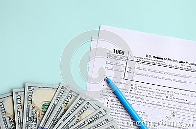 1065 tax form lies near hundred dollar bills and blue pen on a light blue background. US Return for parentship income Stock Photo