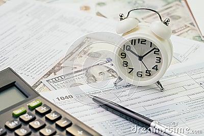 Tax time in April concept, pen on 1040 US individual income tax filling form with alarm clock and US dollar banknotes, deadline Editorial Stock Photo