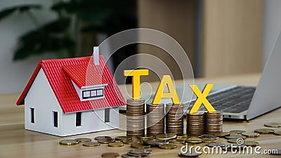 Tax wooden letter on stacked coins with model of house and laptop computer. The concept of paying tax for house and property. Stock Photo