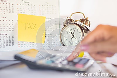 Tax word note on calendar, alarm clock and calculator on table with blur woman hand calculating Stock Photo