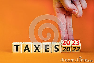 2023 taxes new year symbol. Businessman turns a wooden cube and changes words Taxes 2022 to Taxes 2023. Beautiful orange table Stock Photo