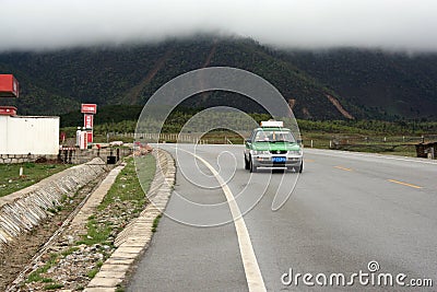 A taxi drives past a petrol station and cloud-covered mountains in south-west China Editorial Stock Photo