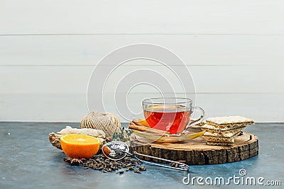 Tea in a mug with herbs, orange, spices, waffle, thread, wooden board, strainer side view on white and stucco background Stock Photo