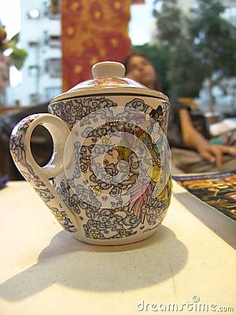 Tea mug with a lid, with beautiful asian painting on it and a finger handle, standing on white table Stock Photo