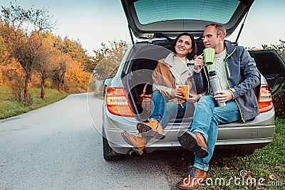 Tea party in car trunk - loving couple drinks hot tea from thermos flask sitting in car trunk Stock Photo