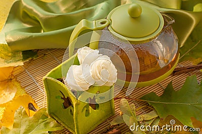 A tea pot, a cup of herbal tea, flowers and autumn leaves Stock Photo