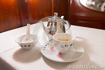 Tea service on a white table : Iron kettle, tea cup with hot tea, a soup bowl & special spoon Stock Photo