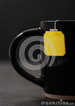Teabag with yellow blank tag of black tea in black ceramic cup on dark board Stock Photo