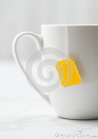 Teabag with yellow blank tag of black tea in white porcelain cup on white Stock Photo