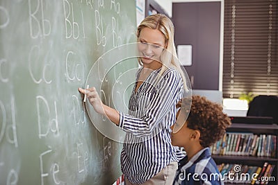 Teacher assisting schoolboy in writing alphabet on chalkboard Stock Photo