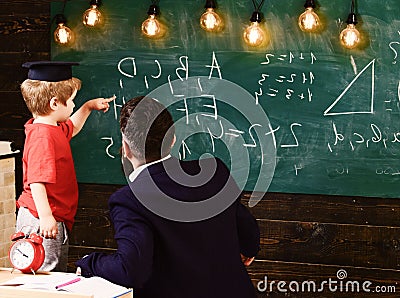 Teacher with beard, father teaches little son in classroom, chalkboard on background. Prodigy child concept. Boy, child Stock Photo