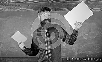 Teacher bearded hipster holds book and laptop. What would you prefer. Teacher choosing modern teaching approach. Paper Stock Photo