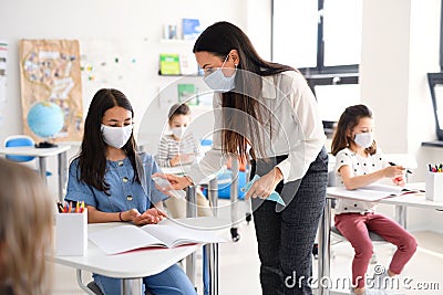 Teacher and children with face mask back at school, disinfecting hands. Stock Photo