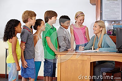 Teacher at desk, students and education with learning for growth and development in classroom. Woman, children and Stock Photo