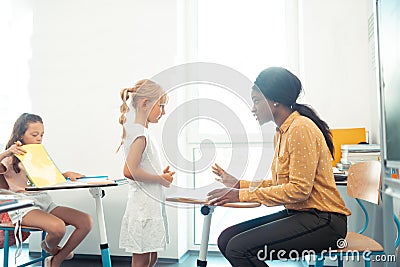 Dark-skinned teacher speaking with cute girl wearing white dress Stock Photo