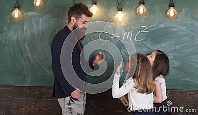 Teacher and girls pupils in classroom near chalkboard. Man with beard in formal suit teaches schoolgirls physics Stock Photo