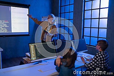 Teacher giving computer science lecture to young students in dark room. Room. Explaining Information Technology. Stock Photo