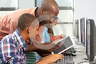 Teacher Helping Boy To Use Digital Tablet In Computer Class Stock Photo