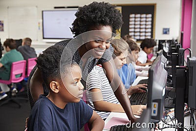 Teacher Helping Female Pupil Line Of High School Students Working at Screens In Computer Class Stock Photo