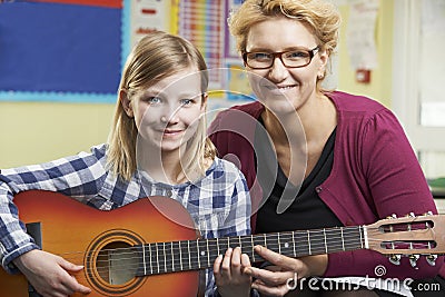 Teacher Helping Pupil To Play Guitar In Music Lesson Stock Photo