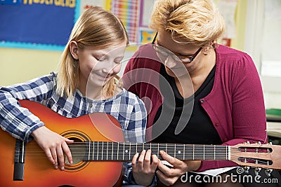 Teacher Helping Pupil To Play Guitar In Music Lesson Stock Photo