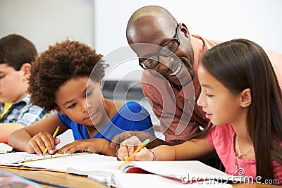 Teacher Helping Pupils Studying At Desks In Classroom Stock Photo