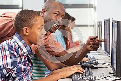 Teacher Helping Students Working At Computers In Classroom Stock Photo