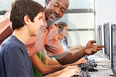 Teacher Helping Students Working At Computers In Classroom Stock Photo