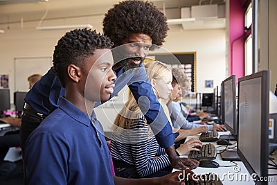 Teacher Helping Teenage Male High School Student Working In Computer Class Stock Photo