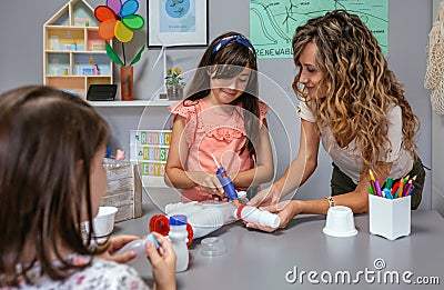 Teacher helping to girl make recycled toy robot with hot melt glue gun Stock Photo